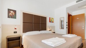 Ein Hotelzimmer mit einem großen Bett, einem Nachttisch, einem kleinen Tisch, einer Holztür und Kunstwerken an den Wänden.
