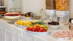 A buffet with various food items including fruits, pastries, and a meat platter.