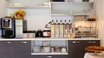 Ein Frühstücksbuffet mit einer Kaffeemaschine, einer Auswahl an Müslis, einem Nutella-Glas und einer Vitrine mit Gebäck.