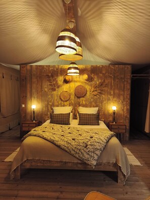 A cozy bedroom with a large bed, two bedside tables with lamps, and a wooden wall with decorative elements. - You & Me Glamping (Moncontour)