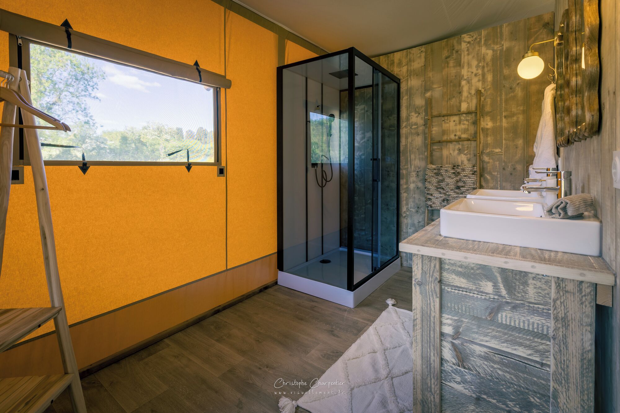 Une salle de bain moderne avec une douche à l’italienne en verre, un plancher en bois et une grande fenêtre.
