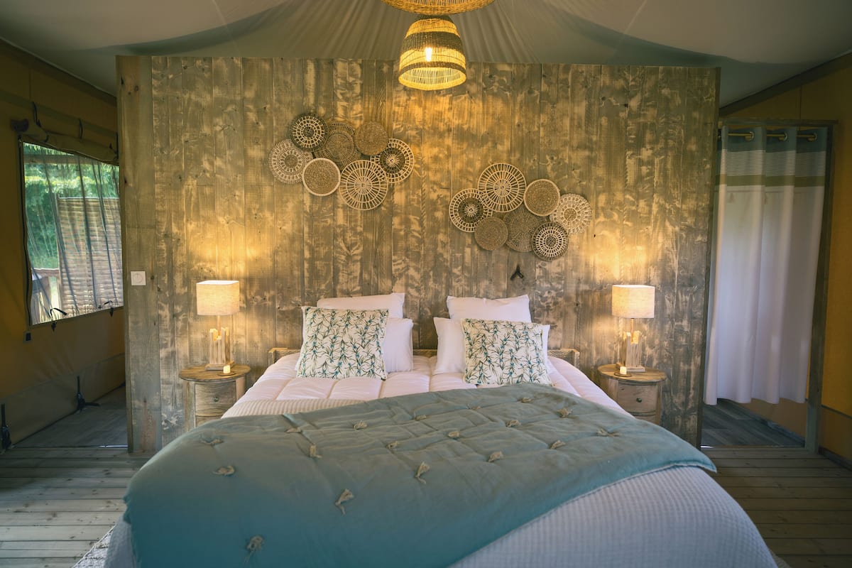 A bedroom with a large bed, two bedside tables, a wall-mounted lamp, and a wooden headboard.