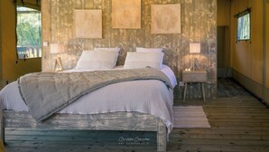Un dormitorio con suelo de madera, una cama con ropa de cama blanca, dos mesitas de noche con lámparas y tres adornos enmarcados en la pared.