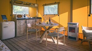 Un cuarto acogedor con piso de madera, una kitchenette pequeña con microondas, un refrigerador y una mesa con sillas. Hay dos ventanas que ofrecen luz natural, y se ve un estufa de leña.