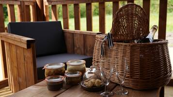 Una terraza de madera con una cesta de mimbre que contiene una botella y copas, tarros de comida y un cuenco de nueces.