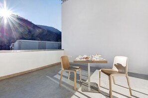 A balcony with two chairs and a table set for dining, overlooking a mountainous landscape.