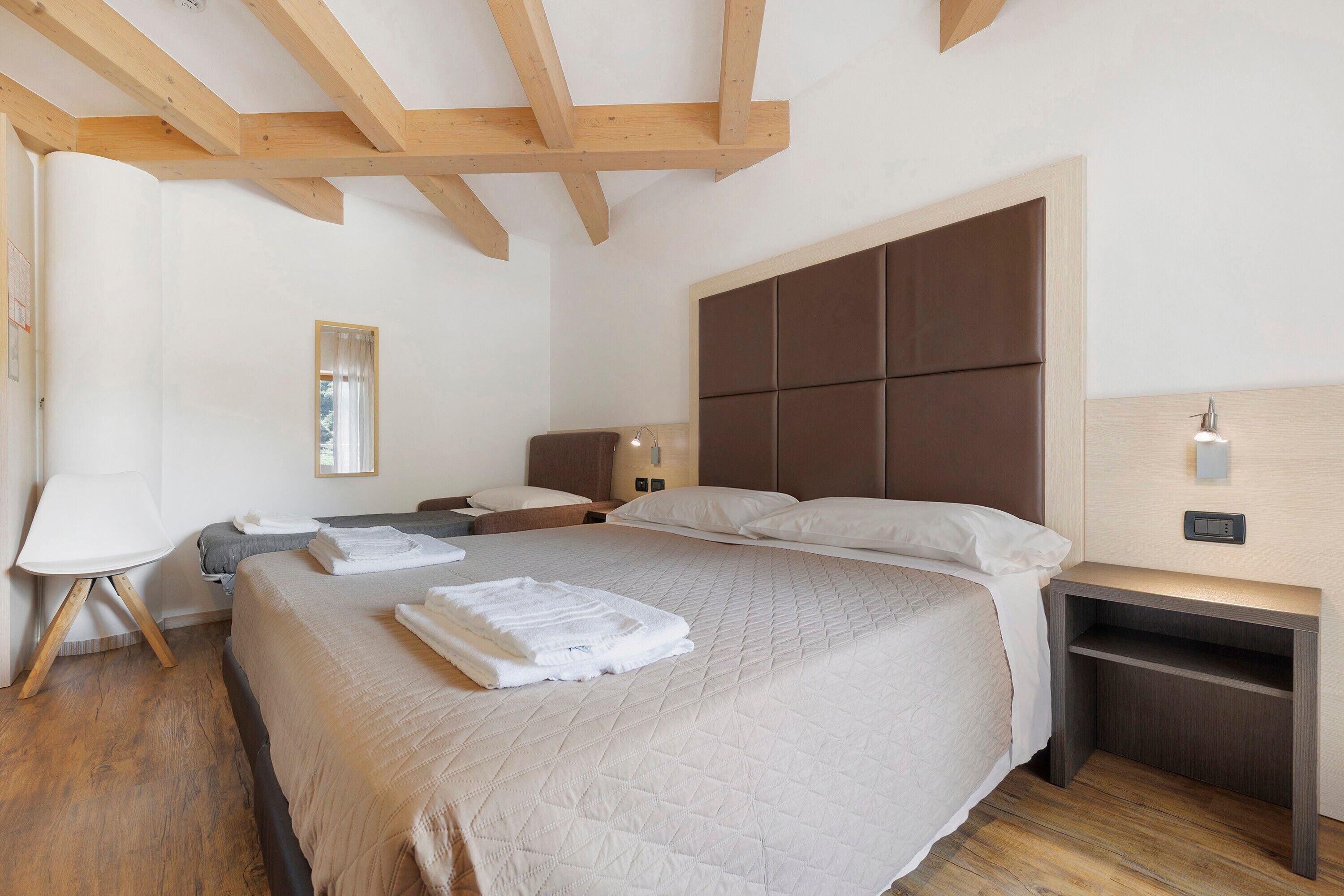 Une chambre d’hôtel avec un grand lit, des poutres en bois au plafond, une table de chevet avec une lampe et une petite table de nuit.
