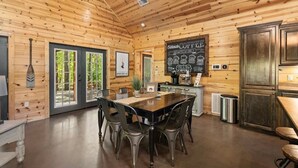 A wooden interior with a dining table, chairs, a chalkboard menu, and a kitchen area. - Creekside Luxury Cabin w/ Hot Tub • Sleeps 12 (Broken Bow)