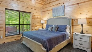 A wooden-paneled bedroom with a bed, two bedside tables, and a window with blinds. - Creekside Luxury Cabin w/ Hot Tub • Sleeps 12 (Broken Bow)