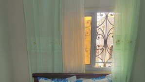 Una cama con una colcha a rayas, dos almohadas con estampado floral y una ventana con reja de metal.