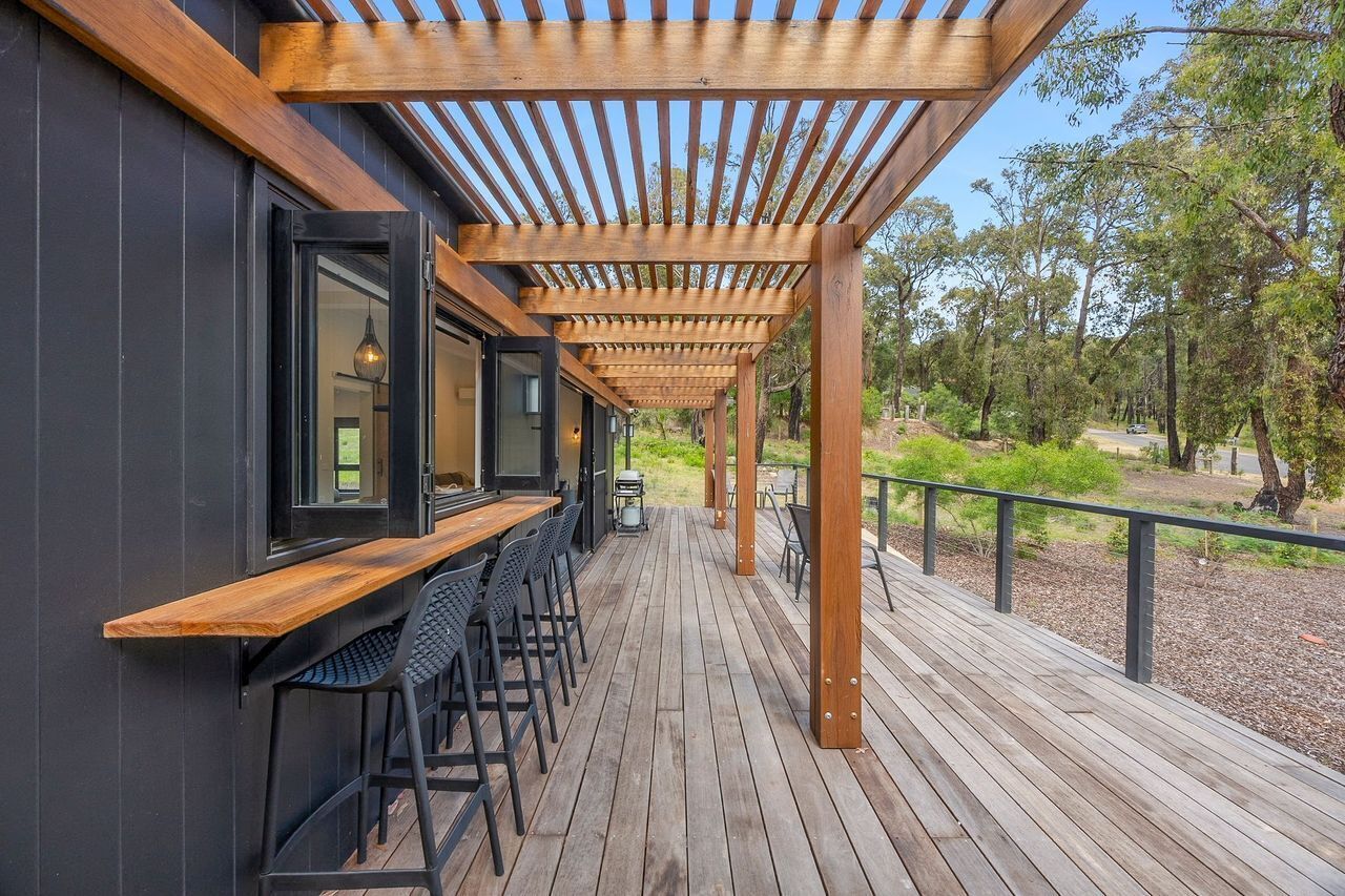 An outdoor wooden deck with a pergola, bar area with stools, and a view of a forested area.