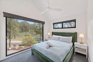 A bedroom with a large window, a bed, two bedside tables, and a ceiling fan. - The Haven on Narani (Fairhaven)