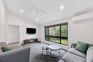 Un soggiorno moderno con televisore a schermo piatto, ventilatore a soffitto, una grande finestra con vista sul verde e un sistema di condizionamento integrato.