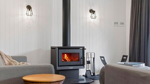 A modern living room with a wood-burning stove, two wall-mounted lights, and a grey sofa.