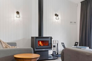A modern living room with a wood-burning stove, two wall-mounted lights, and a grey sofa.