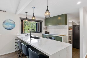 Una cucina moderna con isola centrale, illuminazione a sospensione e vista sul verde attraverso una finestra.