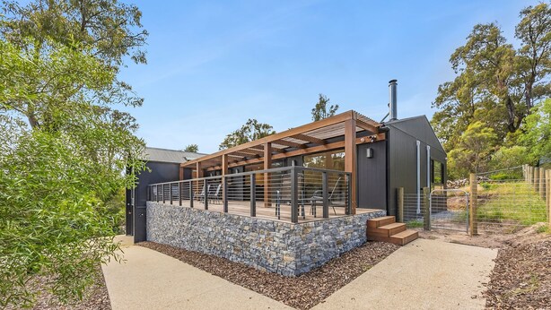 En moderne bygning med stenvæg, træpergola og metalhegn.