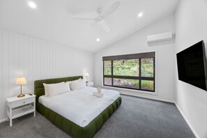 Una camera da letto con un letto, comodini, una ventola a soffitto, un condizionatore d'aria e una finestra vista verde.