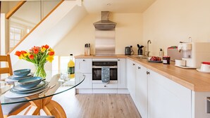 A modern kitchen with a glass dining table, white cabinets, and a stainless steel range hood. - The Stable, Preston, Kent (Preston)