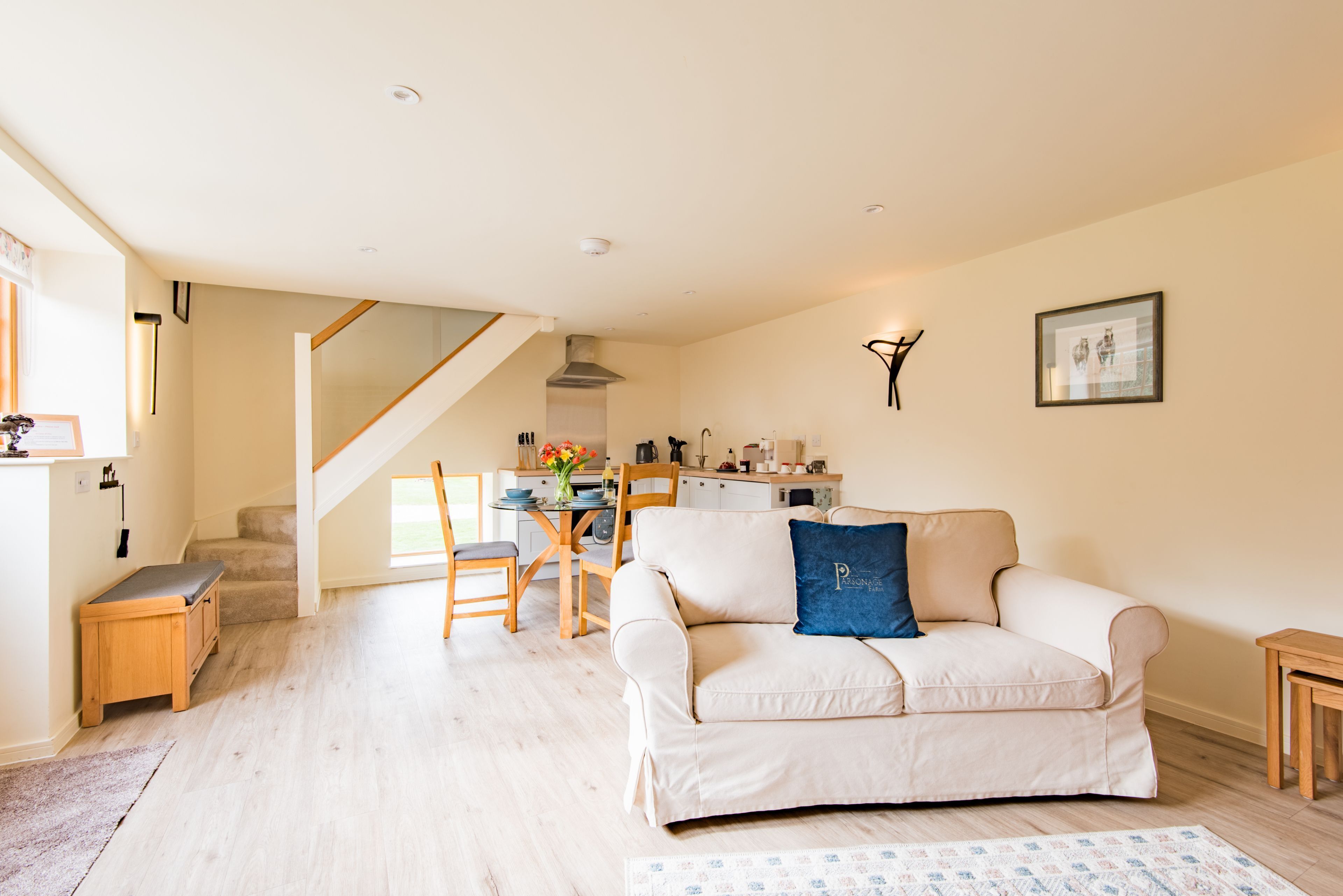 A living room with a sofa, a dining table with chairs, a staircase, and a kitchen area.