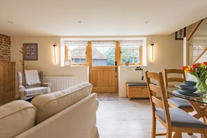 Ein gemütliches Interieur mit einer Couch, einem karierten Sessel, einem Esstisch mit Stühlen und einem Fenster mit Blick nach draußen.