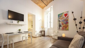 A modern living room with a flat-screen TV, a dining area with a white table and chairs, a sofa, and a large window with a view.