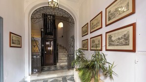 A hallway with a checkered floor, a staircase, and framed pictures on the wall.