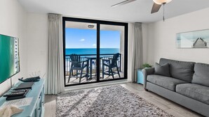 A living room with a grey sofa, a flat-screen TV, a ceiling fan, and a view of the ocean through large sliding doors. - Sundestin 402 (Destin)