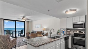 A modern kitchen with white cabinets, a stainless steel oven, and a large island with a sink. There is a balcony with a view of the ocean. - Sundestin 402 (Destin)