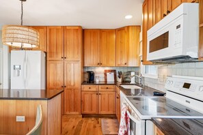A kitchen with wooden cabinets, a refrigerator, a microwave, a stove, and a coffee maker. - Coastal Retreat in South Bethany (South Bethany)
