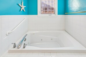 A bathtub with a handrail, a starfish decoration, and a window with frosted glass. - Coastal Retreat in South Bethany (South Bethany)