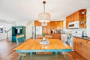 A modern kitchen with wooden cabinets, a dining table with chairs, a chandelier, and a built-in TV. - Coastal Retreat in South Bethany (South Bethany)
