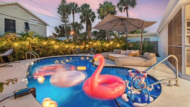 A swimming pool with a pink flamingo float, lounge chairs, and an umbrella. - Walk to Beach- Private Pool • Mini Golf • Firepit (Redington Beach)