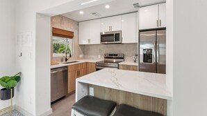 A modern kitchen with white cabinets, stainless steel appliances, and a marble countertop. - Walk to Beach- Private Pool • Mini Golf • Firepit (Redington Beach)