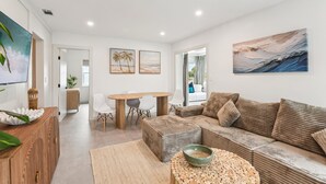 A modern living room with a sofa, a coffee table, and a dining area with a table and chairs. - Walk to Beach- Private Pool • Mini Golf • Firepit (Redington Beach)