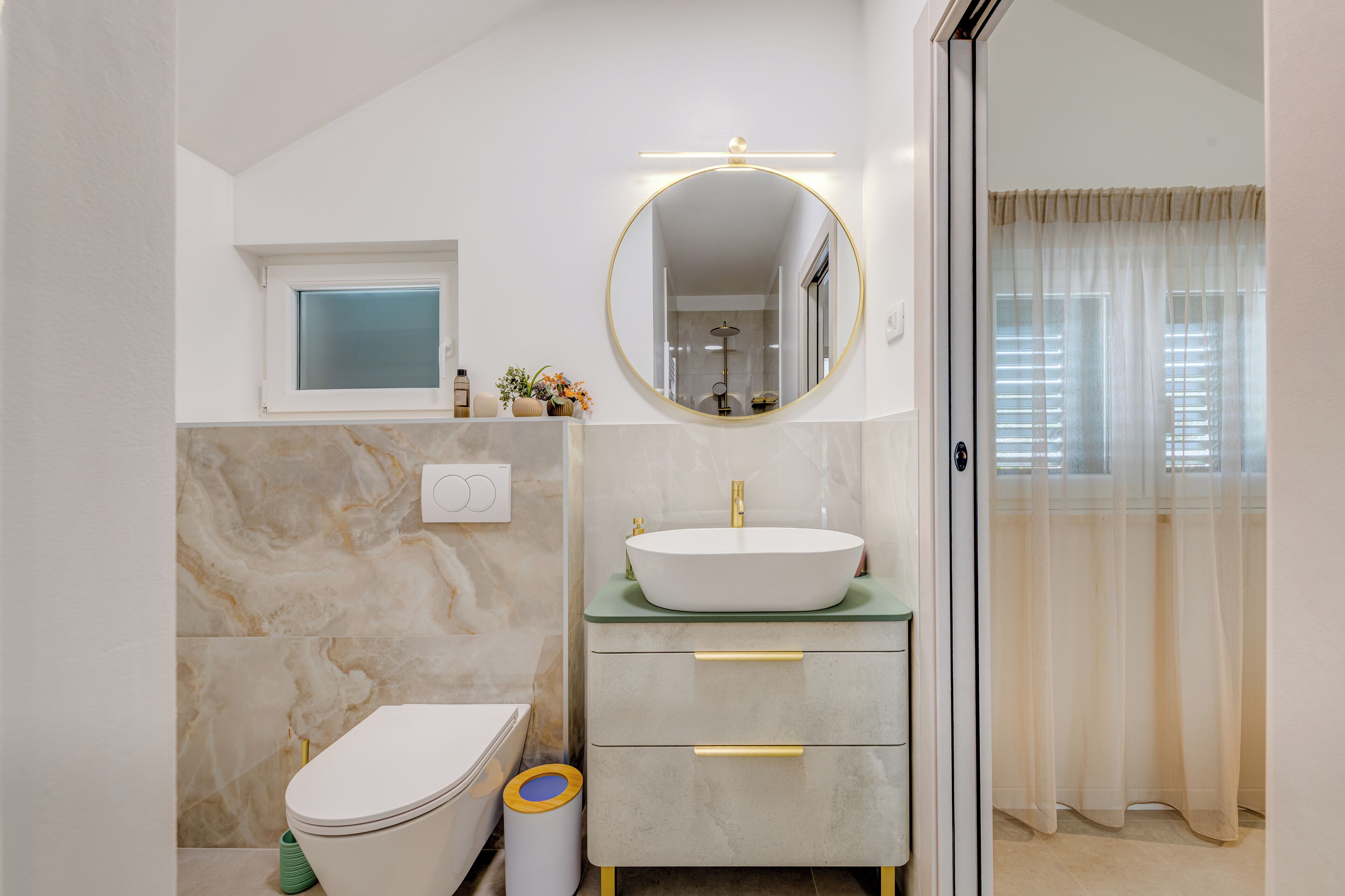 A bathroom with a toilet, sink, mirror, and a window with curtains.