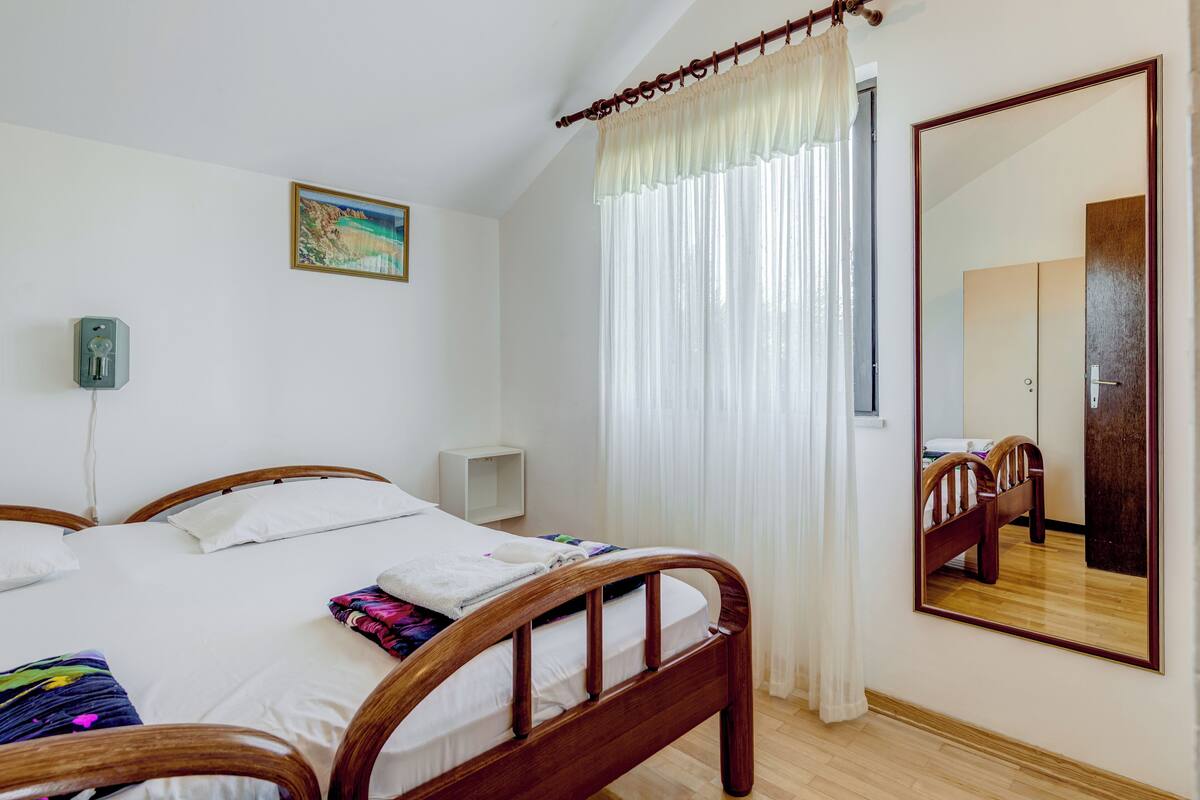 A bedroom with a wooden bed, a bedside table, a mirror, and a window with curtains.