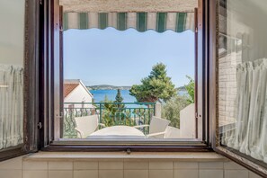 An open window with a view of a balcony, outdoor furniture, and a distant body of water. - 7 Olives Apartments (Rogoznica)