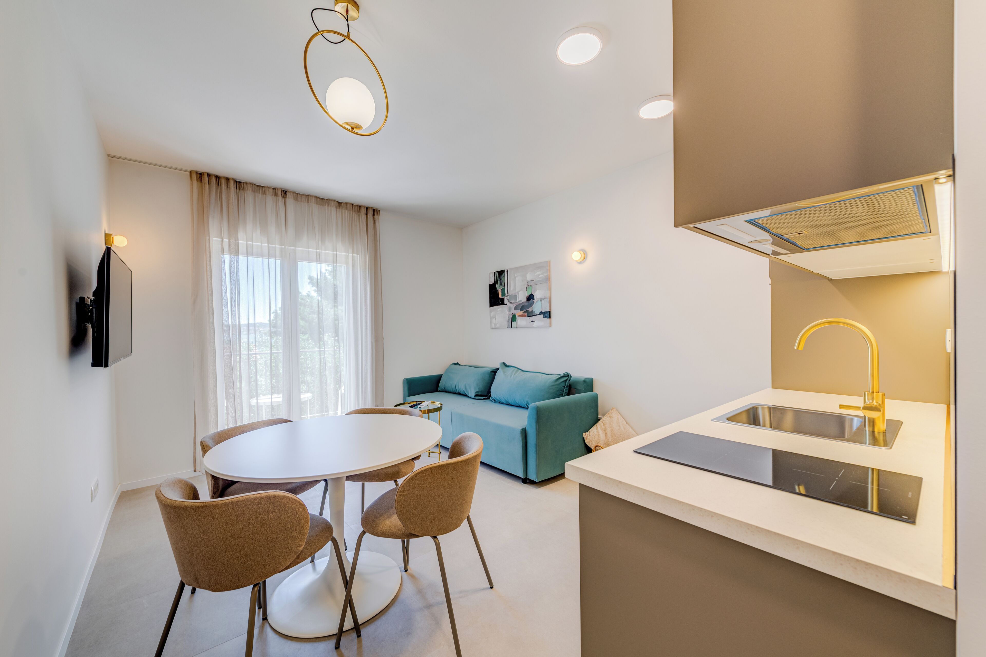 A modern kitchen with a built-in dishwasher, a dining area with a round table and chairs, and a living area with a sofa and a painting.