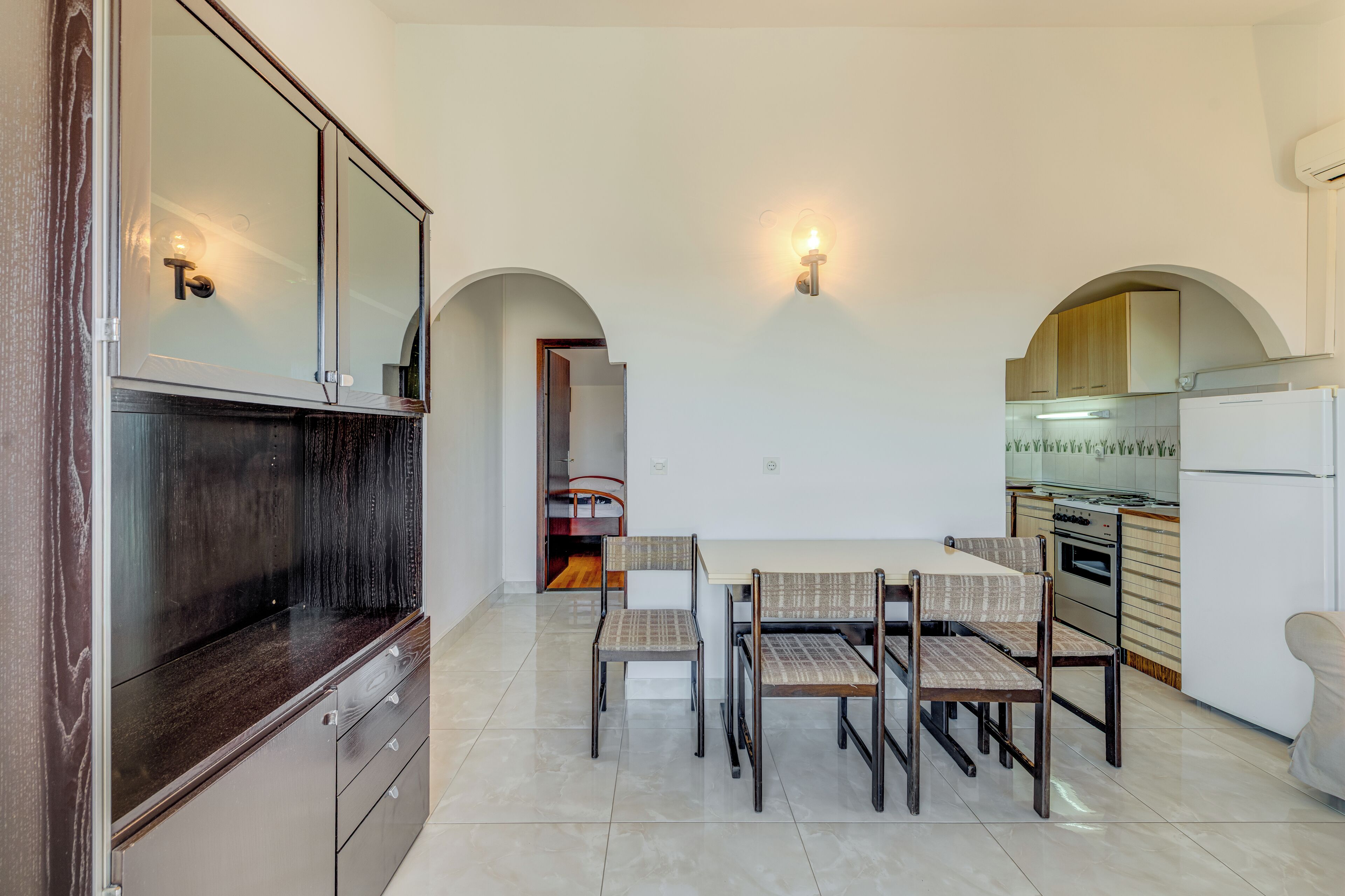 A modern kitchen with a dining area, white walls, and a large window.