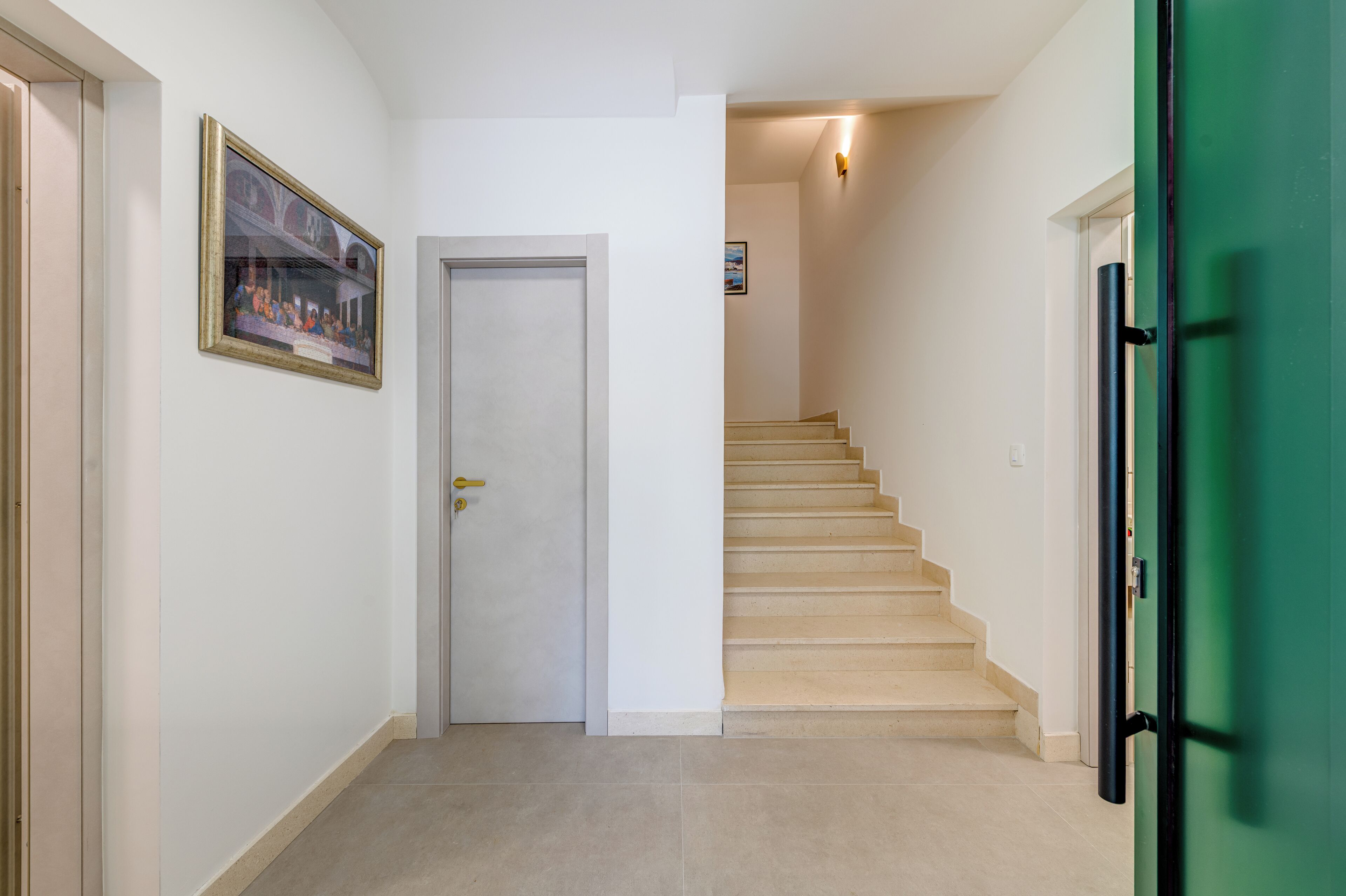 Un pasillo con una puerta blanca, una escalera y una puerta verde.