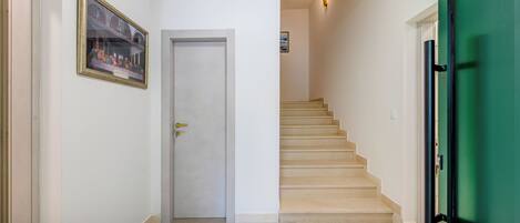Un pasillo con una puerta blanca, una escalera y una puerta verde.