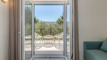A balcony with a table and chairs, a sofa, and a view of trees and a body of water.
