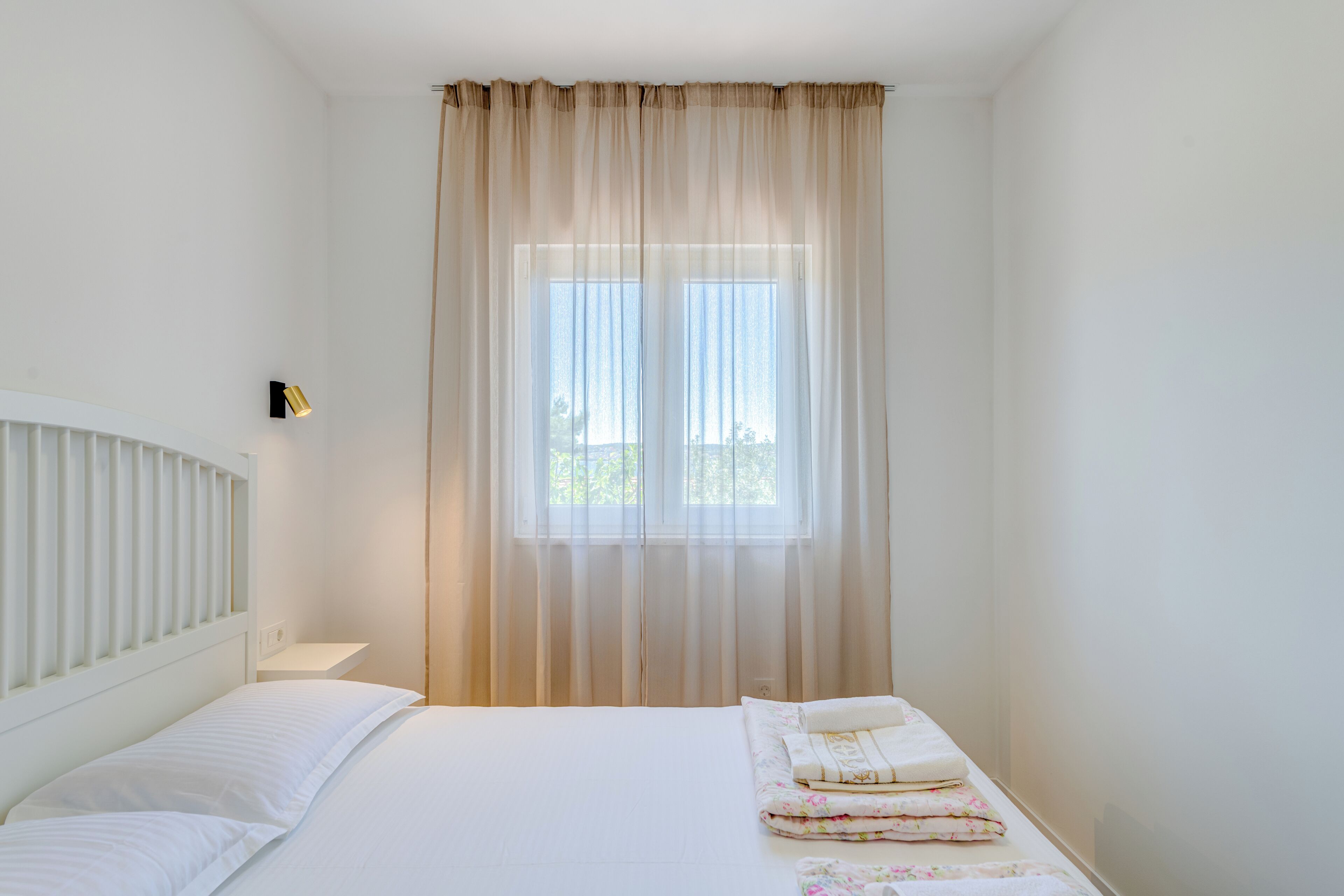 Une chambre à coucher avec un lit, une fenêtre avec des rideaux, une lampe de chevet et une petite table de chevet.