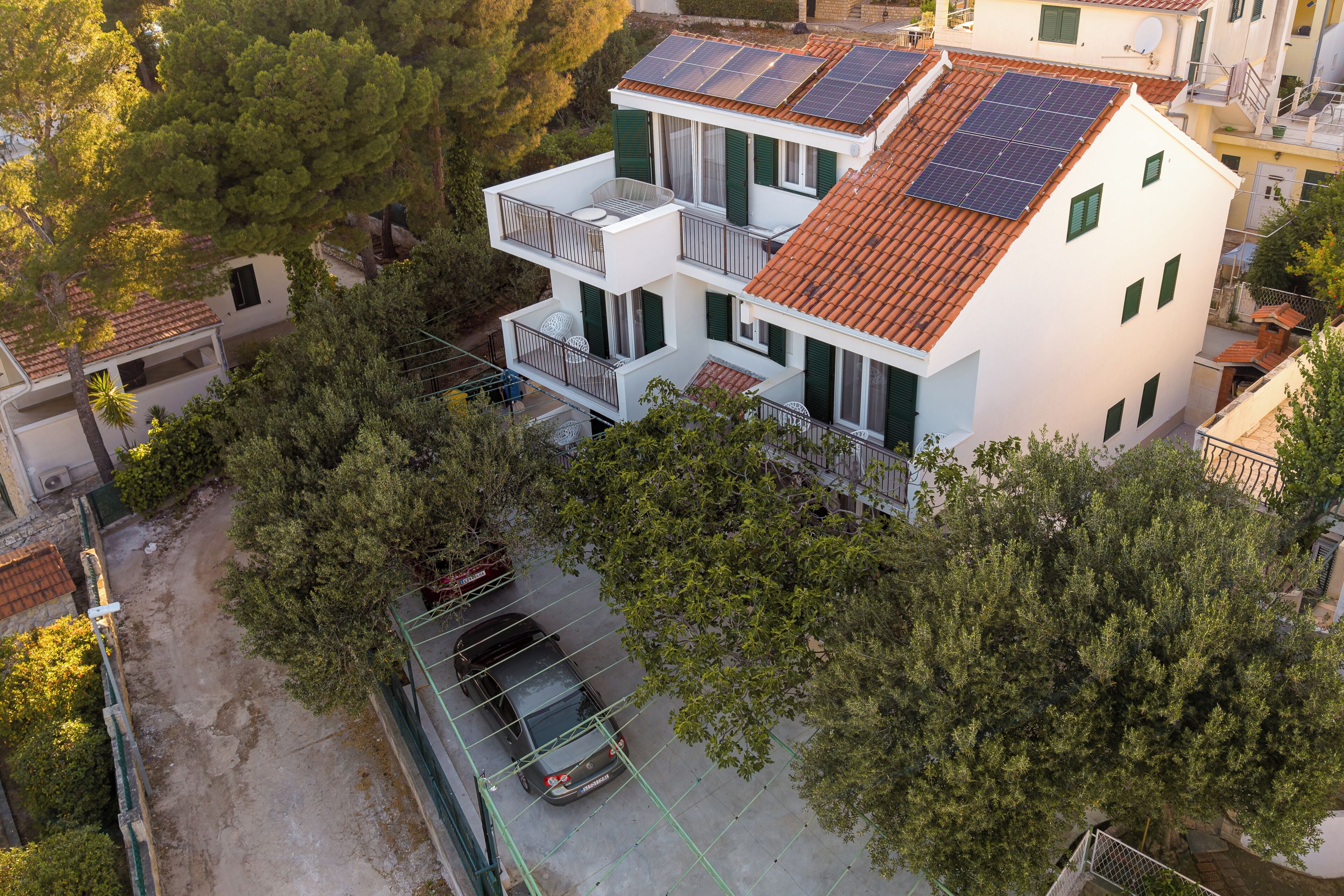 Een meerhoog gebouw met zonnepanelen op het dak, een balkon en een auto ervoor geparkeerd.
