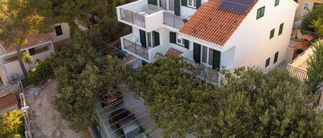 A multi-story building with solar panels on the roof, a balcony, and a car parked in front.
