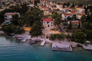 An aerial view of a coastal town with houses, a pier, and a road leading to a central building. - 7 Olives Apartments (Rogoznica)