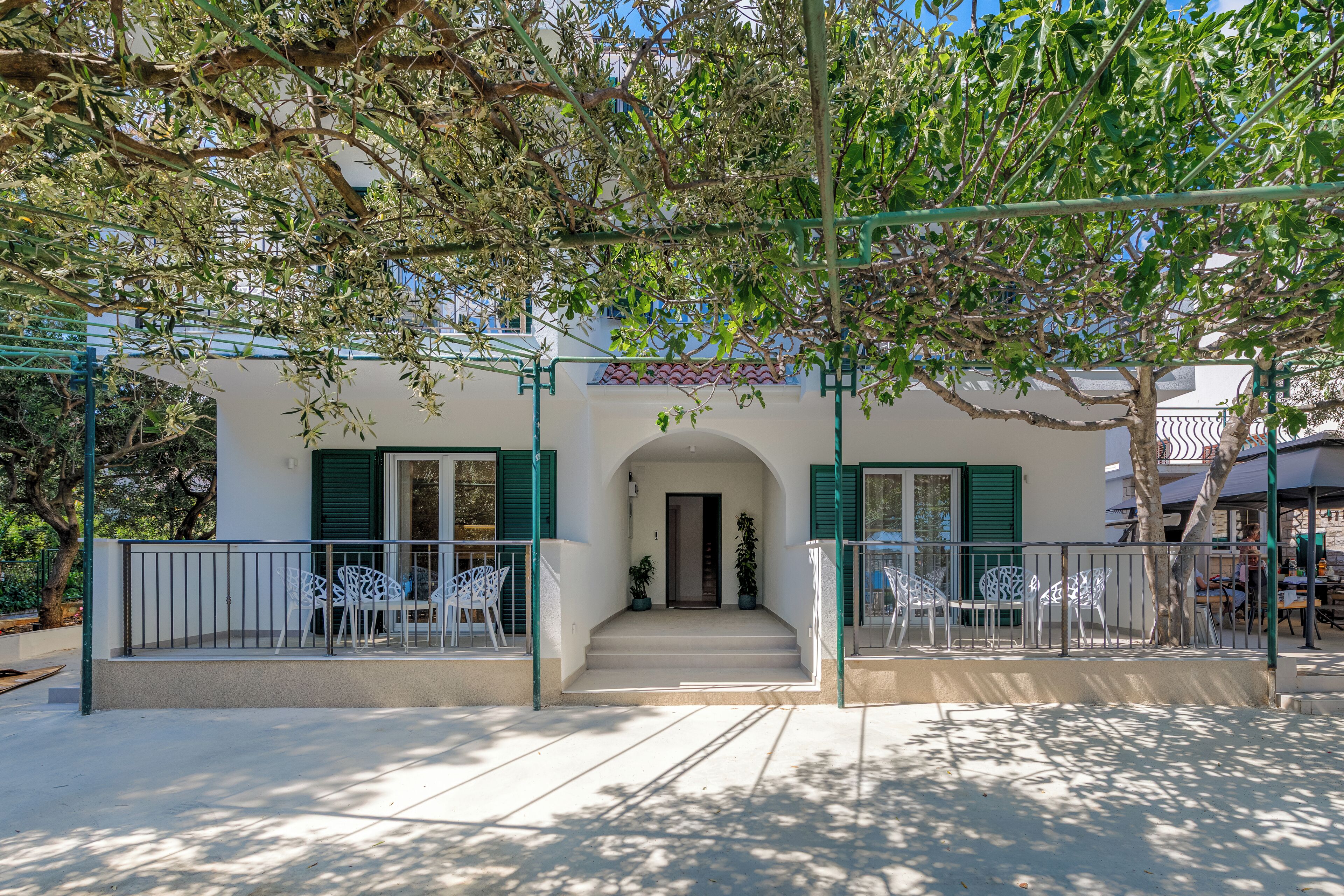 A building with a white facade, green shutters, and a balcony with white chairs.