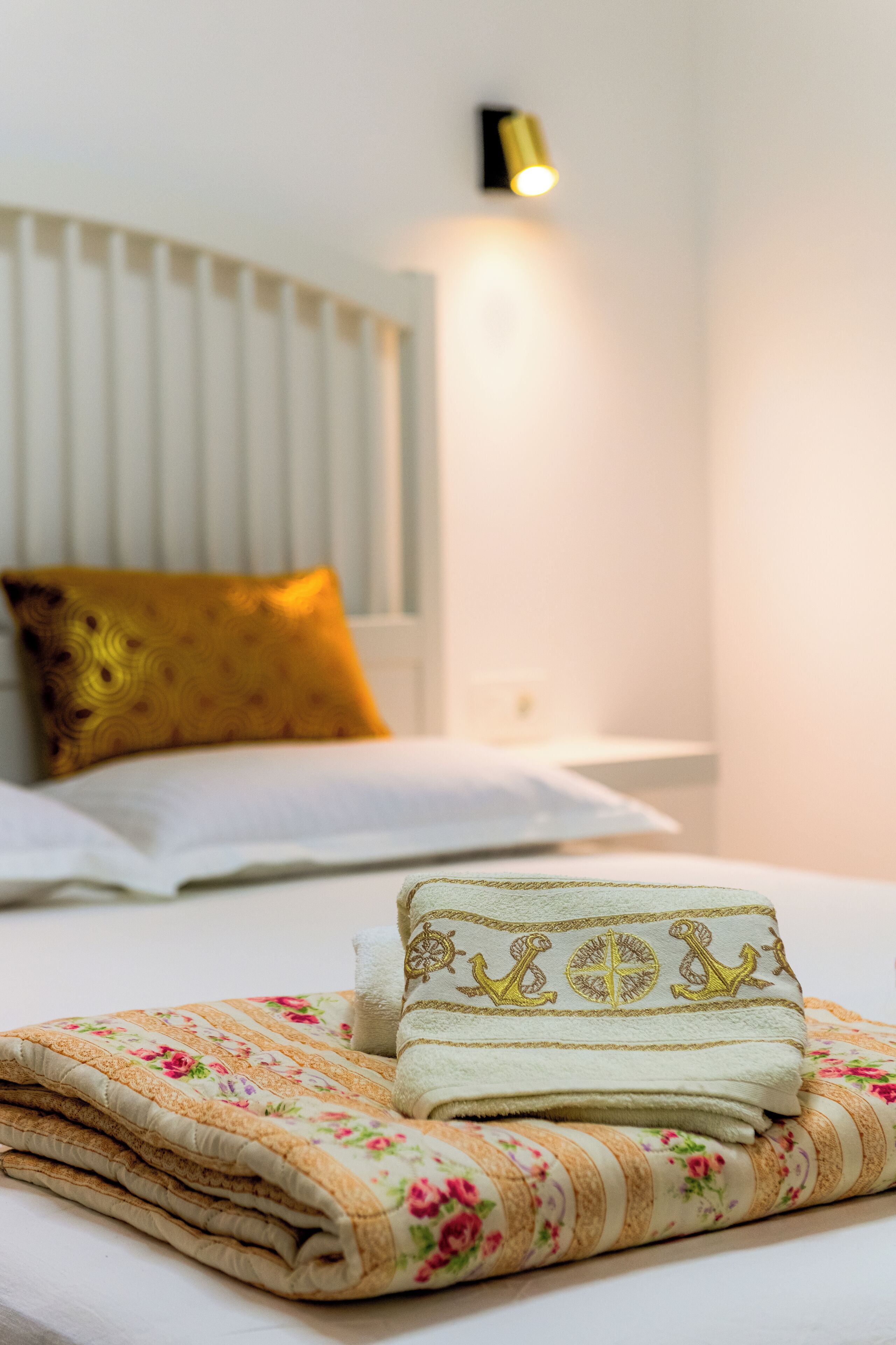 A neatly made bed with a floral-patterned blanket and a folded towel with a decorative design.