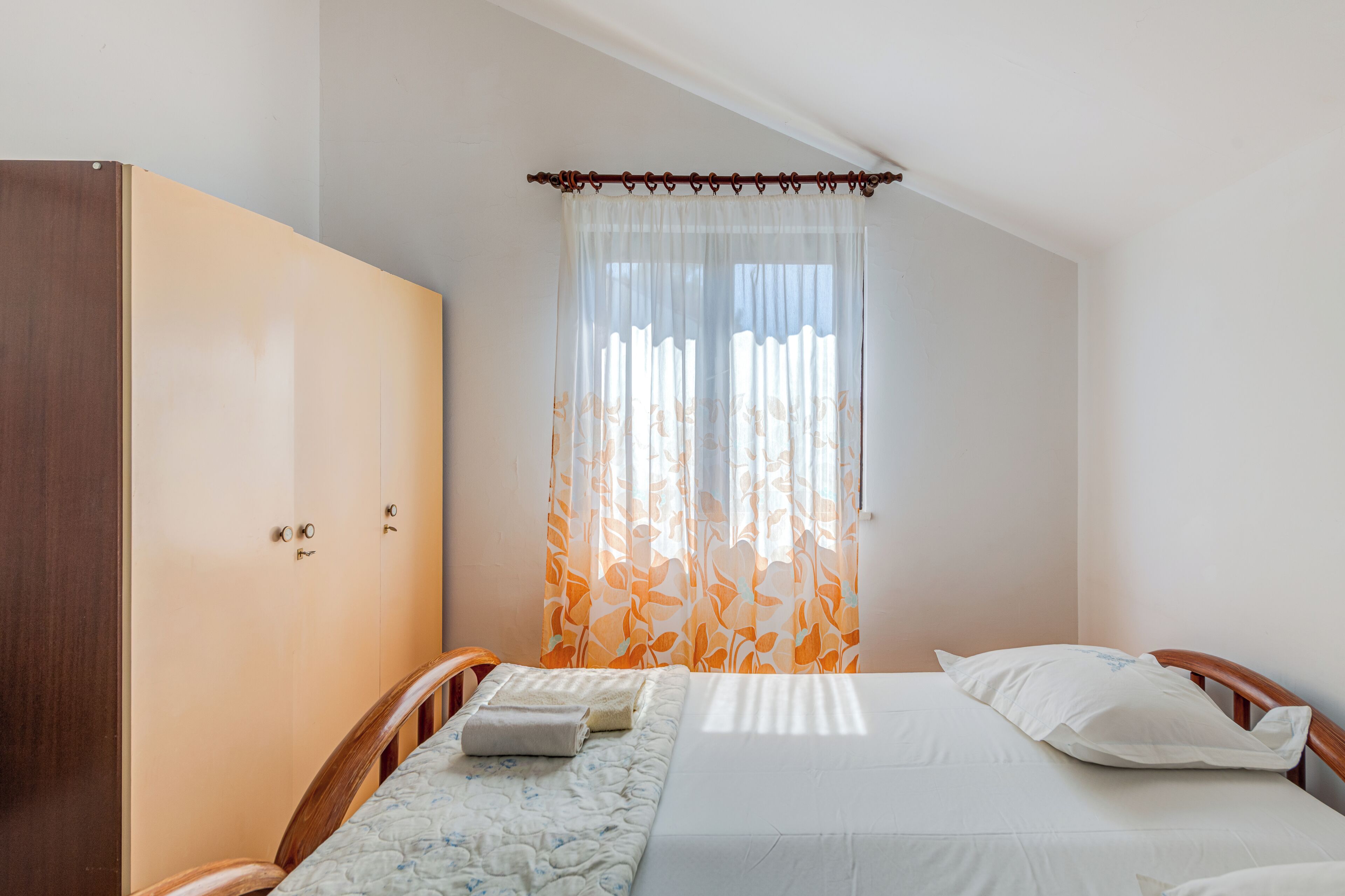 A bedroom with a bed, a wardrobe, and a window with curtains.